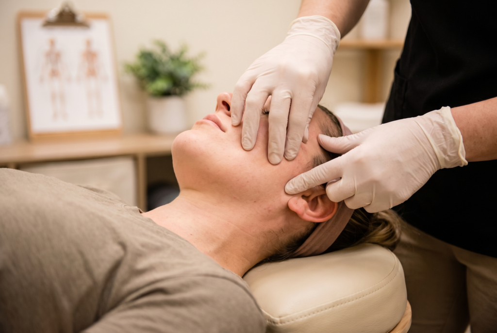 Close-up of a physical therapist examining a patient's jaw and ear area during a TMJ evaluation